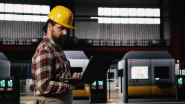 Fabrikada ağır sanayi atölyesinde yürüyen profesyonel mühendis, dizüstü bilgisayarındaki ekipman ve metal iş kalitesini inceliyor. Endüstriyel mühendislik fabrikası üretim.