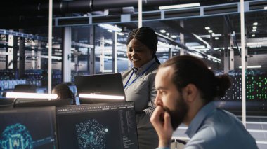 Veri merkezi sistem yöneticisi yazılım güncellemelerini tamamladıktan sonra sinirsel ağ çıktılarından memnun. IT uzmanı gülümsüyor, dizüstü bilgisayara bakıyor, sunucu merkezi donanımı optimize ediliyor, kamera A