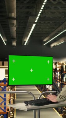 Endüstriyel iş için çeşitli meslektaşların yanındaki monitörde dikey video krom anahtar ekranı var. Bir depoda çalışan adam paket taşıma ve envanter yönetimine odaklanmış. Lojistik verimlilik.