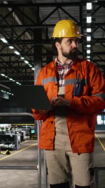Dizüstü bilgisayarda dikey video mühendisi, mekanik sistemleri gözden geçiriyor, büyük endüstri salonu. Mühendislik fabrikasındaki karmaşık üretim süreci için profesyonel çelik işçiliği ve ağır donanım denetimi.