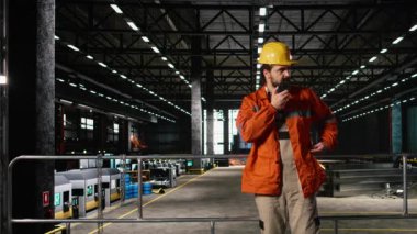 Mühendis, ağır endüstri deposunda sabit şapka takmış taşınabilir telsizle konuşuyor. Kablosuz radyo aygıtı, büyük ölçekli makine salonu boyunca temiz iletişim ve koordinasyon sağlar.