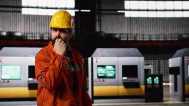 Ağır endüstri operatörü yoğun bir mühendislik fabrikasında telsiz tutuyor. Büyük ölçekli depo çevresi, ağır ekipmanlar ve üretim hattı için gelişmiş radyo teknolojisi..