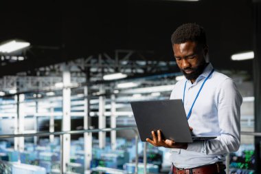 Sanayi platformunda gülümseyen veri merkezi mühendisi nöral ağ yazılım görevleri üzerinde çalışıyor. Neşeli Afro-Amerikan teknisyen büyük dil model mimarisi, teknik destek.