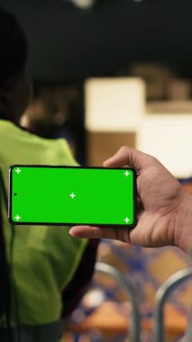 Dikey Video Mobil telefon, yeşil ekran, erkek çalışan, sevkiyat ve sipariş tamamlama, organize raflarla çevrili platformda. Teslimat işlemleri ve güvenlik ile tedarik zinciri kontrolü