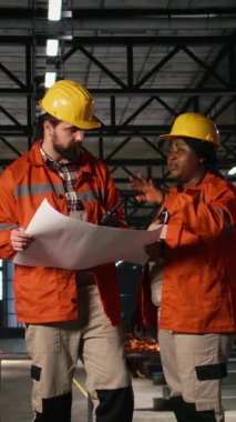 Makine dairesinde planlar ve yerleşim planları üzerinde çalışan mühendislerden oluşan dikey video çeşitliliği. Üretim akışını sağlamak için talimatları ve devreleri kontrol eden erkek ve kadın..