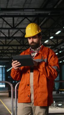 Dikey Video Tesis Mühendisi, tablet, ağır ekipman, büyük endüstriyel alan, mekanik atölye içinde demir atölye ve mühendislik ile denetleme. Sanayi uzmanı üretim hattını güvence altına alıyor.