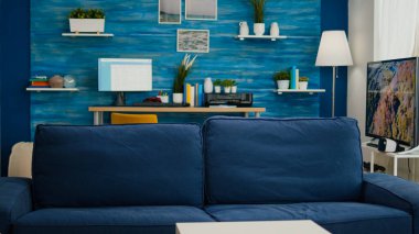 Zarif, parlak oturma odasının içinde çalışma yeri ve arka planda büyük bir televizyon var. Mavi mobilyaları ve duvarları olan boş, modern bir dairede rahat bir kanepe. Güzel dekore edilmiş ve kimse giremiyor.