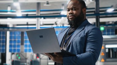 Bir güneş paneli tesisinde Afrika kökenli Amerikalı yönetici performans ve verimlilik ölçümlerini izliyor, gerçek zamanlı kalite kontrolü ve stratejik iş geliştirme ile liderliği birleştiriyor. Kamera B.