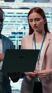 Sunucu merkezindeki dikey video mühendisliği ekibi, makinelerin bakımını yapmak için dizüstü bilgisayarla birlikte çalışıyor. Modern yüksek teknoloji veri merkezinde çalışan takım arkadaşları sunucu ayarlarını yapılandırıyor