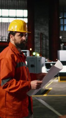 Dikey Video Mühendisi tesis boyunca yürüyor üretim planlarını, teknik planlarını, ağır sanayi deposunu inceliyor. Üretim salonu makine talimatları, düzen çizimleri içerir.