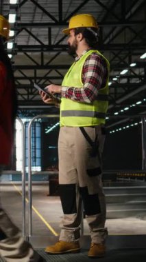 Dikey Video Mekanik uzmanı, ağır ekipmanları inceliyor, tablet üzerinde performans, yoğun fabrika içi. Büyük makineler ve çelik işleri endüstri salonunu domine ediyor ve büyük ölçekli destekliyor.