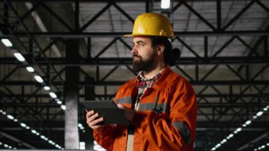 Mühendislik fabrikası işçisi, başlık, ağır sanayi, üretim hattını sağlama, depoda tablet kullanımı. Metal ve endüstriyel ekipmanlarla büyük ölçekli üretim süreci.