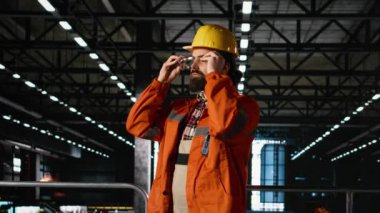 Kasklı ve güvenlik gözlüklü personelin portresi makine dairesinde endüstriyel tasarımı inceliyor. Ağır çelik kirişler ve metal işçiliği ağır sanayi deposunu ve mühendislik uzmanlığını tanımlıyor.