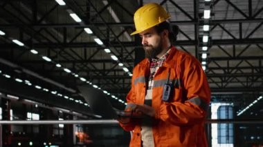 Metalik iskeleti, mühendislik fabrikasında ve ağır sanayide inceleyen sağlam şapkalı bir mühendis. Üretim salonu bünyesindeki büyük ölçekli makine ve çelik çalışmaları üretim sürecini ön plana çıkarıyor.