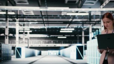 Modern yüksek teknoloji sunucu merkezinde bir kadın altyapı makinelerinde bakım işleri için defter kullanıyor. Veri Merkezi kadın mühendis sunucu ayarlarını dizüstü bilgisayar, kamera B ile yapılandırıyor