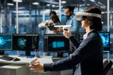 VR kulaklık kullanarak veri merkezi geliştiricisi, AI model parametrelerini sistemleri yükseltmek için ayarlıyor. Sanal gerçeklik kullanarak sunucu odasında bilgi işlem uzmanı, donanım donanımları için derin öğrenme kontrolü ayarlanıyor