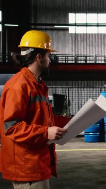 Dikey Video Adam mühendisi, planlar, çizimler ve yerleşim planları, makine dairesi üzerinde çalışıyor. Metal işçiliği, ağır ekipman ve üretime rehberlik eden ileri teknoloji ile dolu sanayi bölgesi