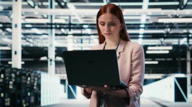 Sunucu çiftliğinde çalışan gülümseyen bir kadının portresi ağ yönetimi viralizasyonu yapıyor. Neşeli veri merkezi kadın teknisyeni laptop ile büyük ölçekli bilişim altyapı süper bilgisayarlarını denetliyor.