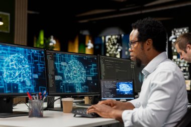 Yapay zeka otomasyonunu kullanarak program geliştirmek için teknoloji firmasındaki bilgisayarı kullanan bir yönetici. Afrika kökenli Amerikalı bilişim uzmanı bilgisayar üzerinde çalışıyor, yapay zeka ile uygulamaları hata ayıklıyor