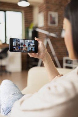 Uzaktan kumandalı kadın cep telefonuyla grup video görüşmesine katılıyor. Ofis brifinginde çok ırklı bir ekiple işbirliği yapıyor. Sanal hissedarlar toplantısına katılan serbest çalışan kadın.