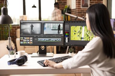 Daireden çalışan bir bayan kameraman, film görüntülerini masaüstü monitörlerinde birleştiriyor. Dijital ortam ve özel efektler üretmek için profesyonel düzenleme yazılımı kullanan odaklanmış kadın düzenleyici.