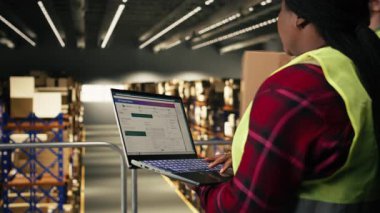 Afrikalı Amerikalı çalışan, izleme yazılımı, depoda dizüstü bilgisayar, platformda durmak ve siparişin yerine getirilmesini sağlamak. E-ticaret dağıtımı için havayolu fatura etiketleri.