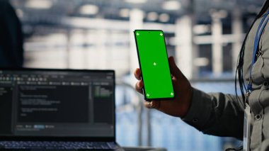 Mühendis, derin öğrenme sistemlerini optimize ederken sunucu odasında izole ekran akıllı telefonu kullanıyor. Veri merkezi çalışanı krom anahtar cep telefonu kullanıyor, Yapay zeka model parametrelerini ayarlıyor, kamera B