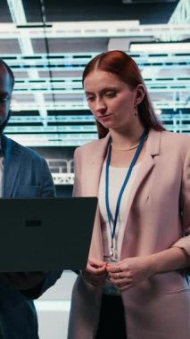 Sunucu merkezindeki dikey video mühendisliği ekibi, makinelerin bakımını yapmak için dizüstü bilgisayarla birlikte çalışıyor. Modern yüksek teknoloji veri merkezinde çalışan takım arkadaşları sunucu ayarlarını yapılandırıyor