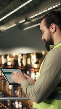 Vertical Video Industrial çalışanı dağıtım merkezindeki tablet üzerindeki havayolu takip bilgilerini kullanarak nakliye için ekspres teslimat paketini gözden geçiriyor. Tamamlama Merkezi