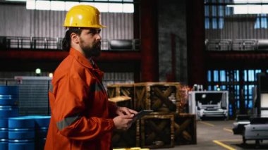 Mühendislik uzmanı büyük ölçekli depo fabrikasındaki operasyonları tablet kullanarak ve ağır ekipmanların yanında yürüyerek izliyor. Sanayi dairesi altyapı için verimli makineler sağlıyor.