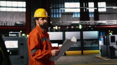Mühendis tesiste yürüyor. Üretim planlarını, teknik planlarını, ağır sanayi deposunu inceliyor. Üretim salonu makine talimatları, düzen çizimleri içerir.
