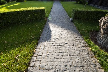 Güneşli bir günde çimlerle ve çalılarla çevrili doğal taş patika.
