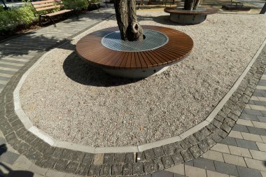 Peyzaj parkındaki bir ağacın etrafında tahta koltuklar.