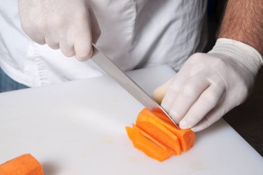 Eldivenli şef plastik bir tahtanın üzerinde havuç keser.