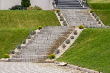 Çevre düzenlemesindeki yeşil boxwood çalılarının arasından yükselen granit adımlar.