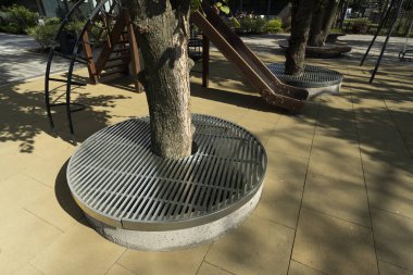Parktaki ağaçların yanında metal ızgaralar ve oyun parkında peyzaj.