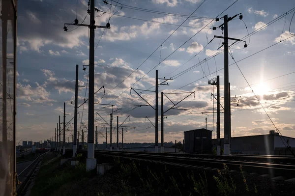 Günbatımında gökyüzüne karşı elektrik kablolarıyla direkler, demiryolu siluetleri