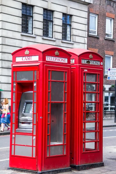 Two red phone booths on the street. One of the booths converted into ATM. London, UK