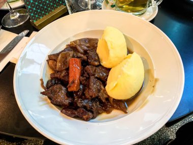 Beyaz tabakta patates püresi ve havuçla servis edilen sığır eti güveci..