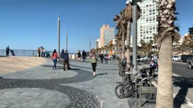 Tel Aviv, İsrail - 09 Mart 2019: Akdeniz Gordon plajı, güneşli bir bahar gününde arka planda mavi gökyüzü ve lüks oteller ve etrafta yürüyen insanlarla dolanıyor. 4K