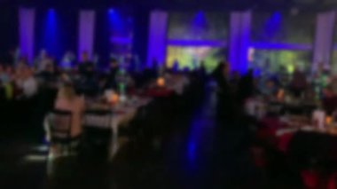 Bir grup siluetli insan (misafirler) düğün resepsiyonu için masalardaki karanlık bir ziyafet salonunda. Bulanık görüş. 4K