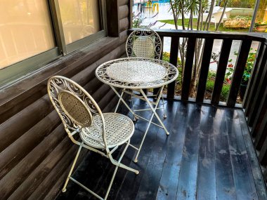 Two white metal chairs and a small round table on a brown wooden terrace. Series of furniture.