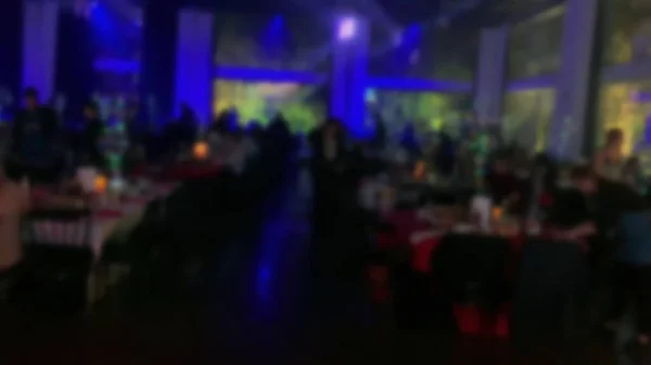 Group of silhouetted people (guests) in a dark banquet hall at the tables for a wedding reception. Blurred view.