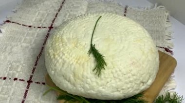 Yuvarlak, beyaz ev yapımı peynir. Adighe peyniri ve ahşap tahtada duran yeşiller. 4K