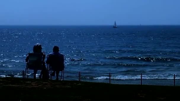 傍晚时分 老人和妇女在微微汹涌大海的背景下 坐在折叠椅上休息 — 图库视频影像