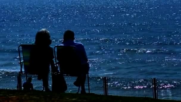 傍晚时分 老人和妇女在微微汹涌大海的背景下 坐在折叠椅上休息 — 图库视频影像