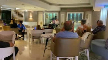 Ölü deniz, İsrail - 7 Mayıs 2021: Otel lobisinde akşam dinlenmesi. Otel konukları müzisyenin performansını dinliyor. HD