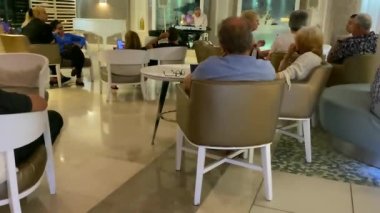 Ölü deniz, İsrail - 7 Mayıs 2021: Otel lobisinde akşam dinlenmesi. Otel konukları müzisyenin performansını dinliyor. HD