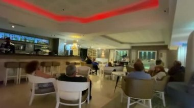 Ölü deniz, İsrail - 7 Mayıs 2021: Otel lobisinde akşam dinlenmesi. Otel konukları müzisyenin performansını dinliyor. HD