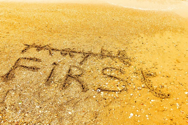 La palabra PRIMERO escrito en una playa de arena en negrita . —  Fotos de Stock